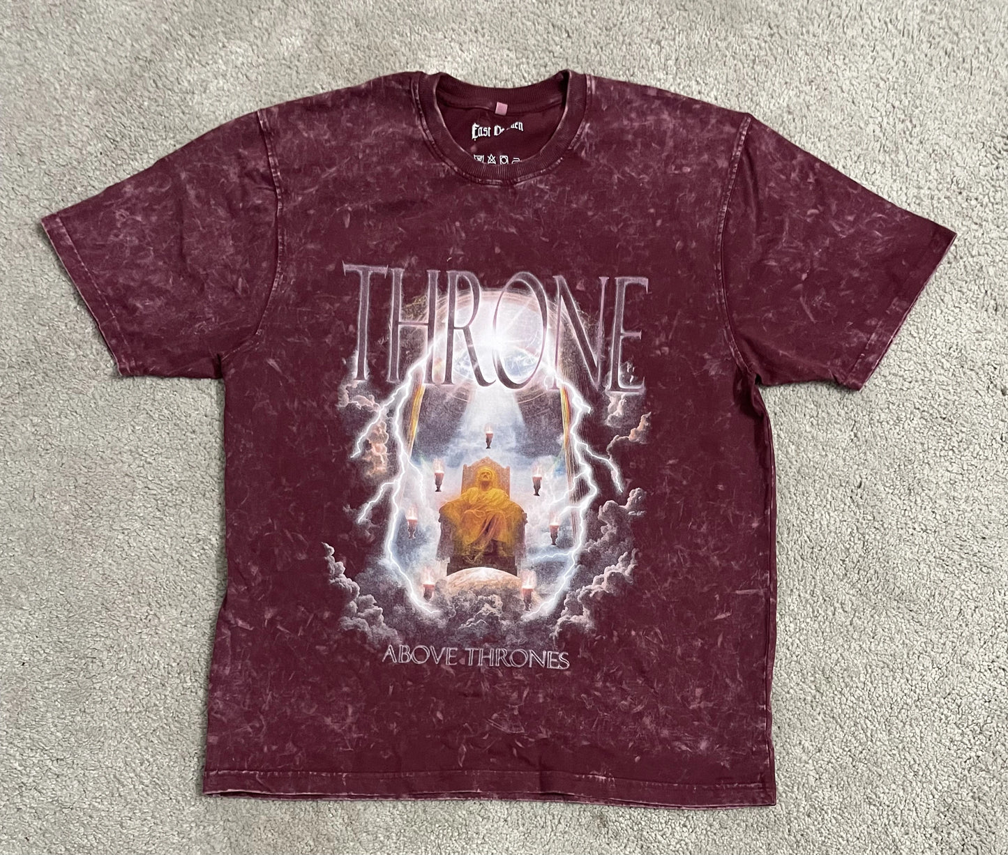 Maroon acid-washed t-shirt featuring a dramatic illustration of the heavenly throne from Revelation, with a robed figure seated in light, surrounded by lightning and seven flaming torches, paired with bold text reading “Throne” and “Above Thrones.” A key piece in the grunge Indian Christian streetwear collection.