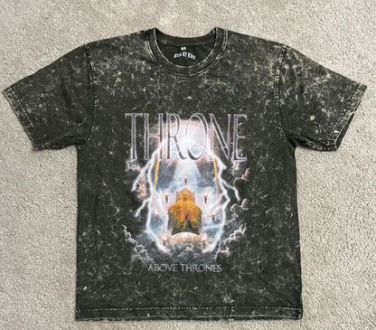 Olive green acid-washed t-shirt featuring the “Throne Above Thrones” graphic inspired by Revelation, showing a radiant enthroned figure surrounded by lightning and clouds, laid flat on a gray surface. A striking piece from the grunge Indian Christian streetwear collection.