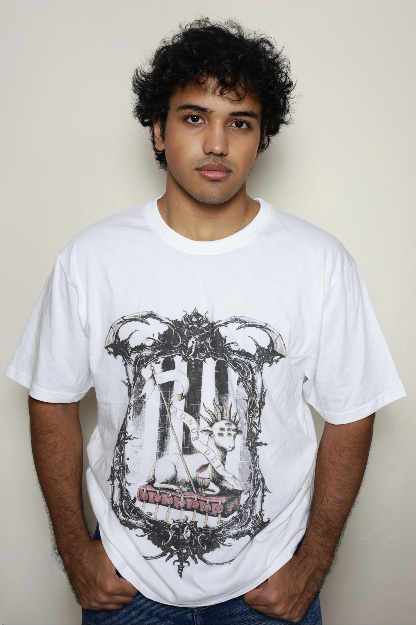 White oversized t-shirt worn by a model, featuring the “Agnus Dei” design: a lamb with seven eyes and horns seated on the Book with Seven Seals, framed by ornate gothic elements — part of your grunge Indian Christian streetwear line.