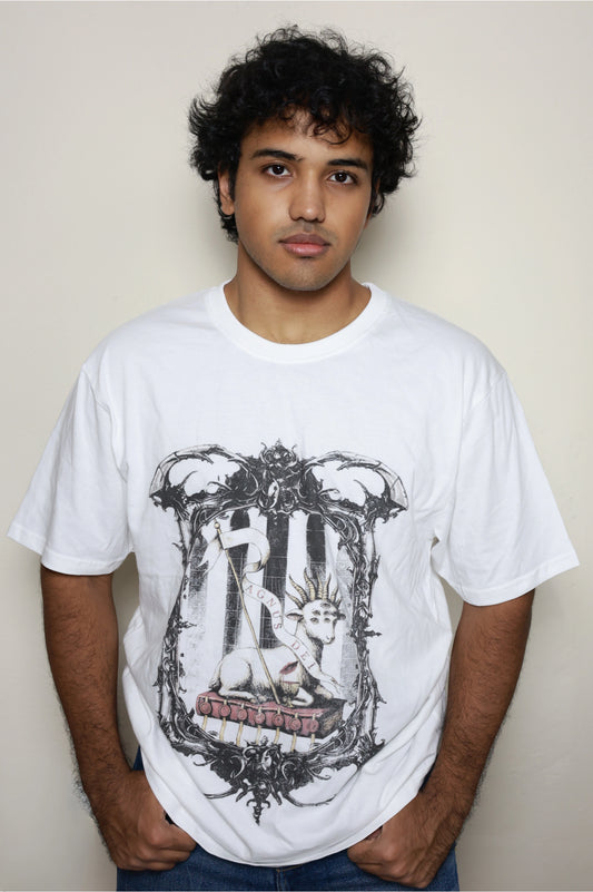 White oversized t-shirt worn by a model, featuring the “Agnus Dei” design: a lamb with seven eyes and horns seated on the Book with Seven Seals, framed by ornate gothic elements — part of your grunge Indian Christian streetwear line.