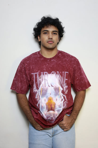 Model wearing a maroon acid-washed t-shirt featuring the “Throne Above Thrones” graphic from Revelation, with a radiant figure seated on a heavenly throne surrounded by lightning and seven flames. A bold piece from the grunge Indian Christian streetwear collection.